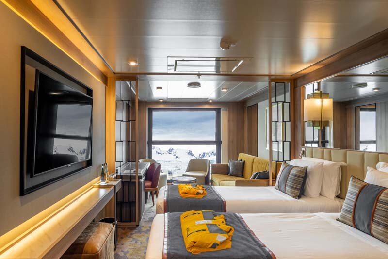 Infinity Suite auf der World Explorer mit zwei Betten, Expeditionsparkas, großem Panoramafenster und arktischer Aussicht.