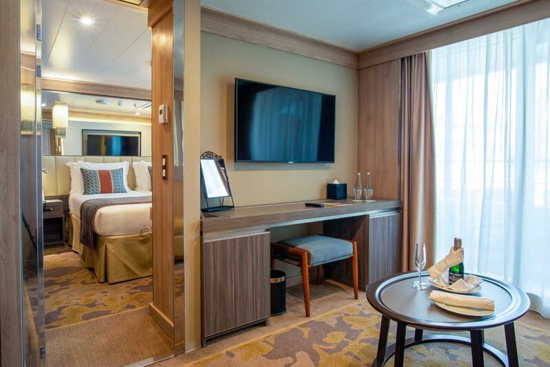 Owner's Suite auf der World Explorer mit Wohnbereich, Fernseher, Schreibtisch und Blick in den angrenzenden Schlafbereich.