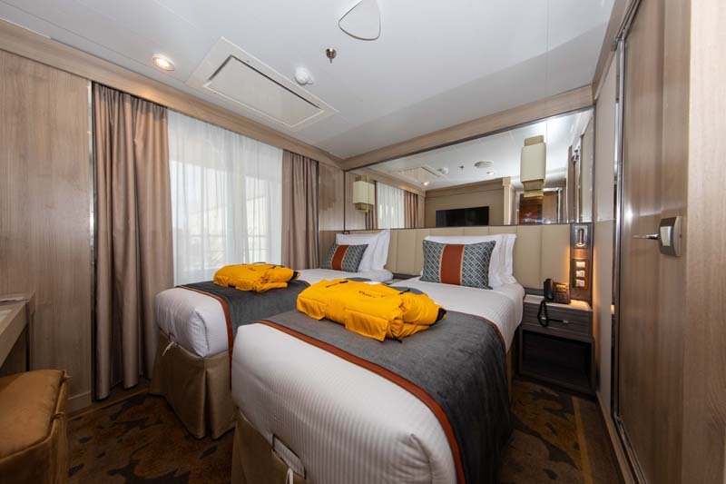 Superior Suite auf der World Explorer mit zwei Betten, gelben Expeditionsparkas und großem Spiegel-Schrank.