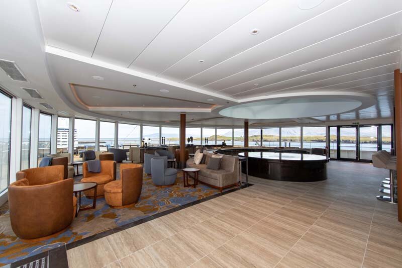 Observation Lounge auf der World Explorer mit Panoramaverglasung, Sesseln in Bernsteinfarbe und zentraler Rundbar.