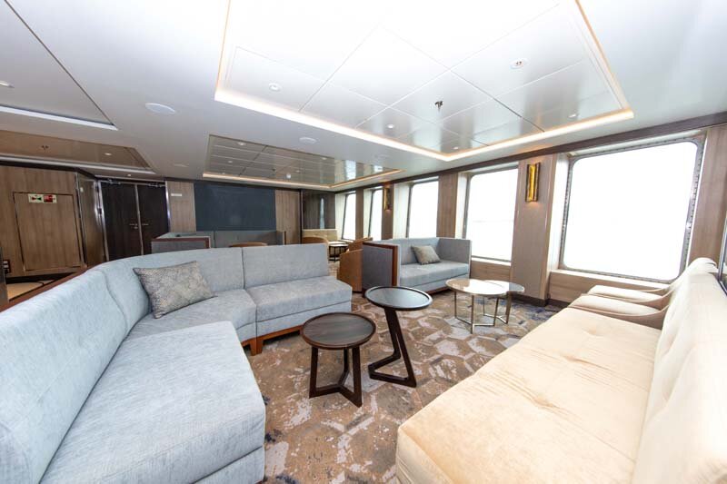 Explorer Lounge auf der World Explorer mit geschwungenen Sofas, Couchtischen und großen Panoramafenstern.