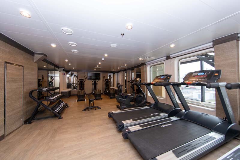 Fitnessstudio auf der World Explorer mit Laufbändern, Crosstrainern und weiteren Trainingsgeräten sowie Spiegelwand.