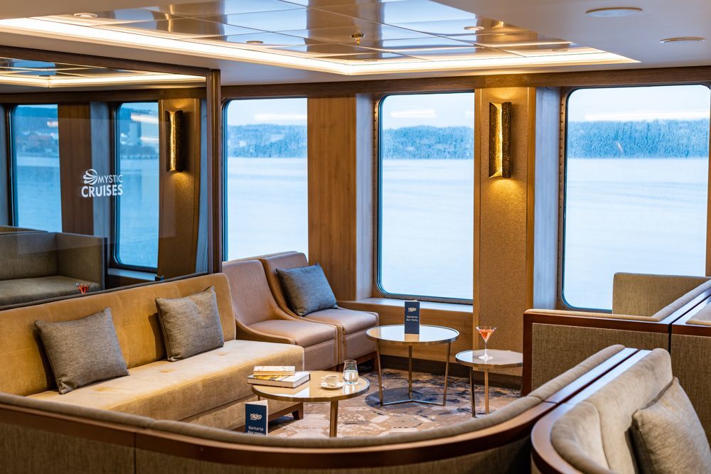 Gemütliche Lounge mit Sofas, Sesseln und Panoramafenstern mit winterlicher Landschaft auf einem Expeditionsschiff