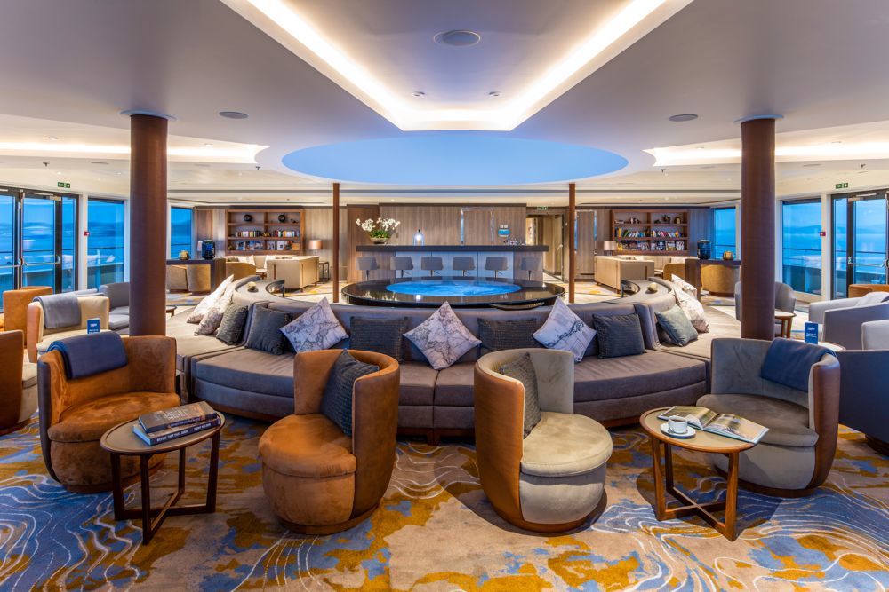 Observation Lounge der World Voyager mit runder Mittelsofa, Panoramafenstern und Bücherregalen.